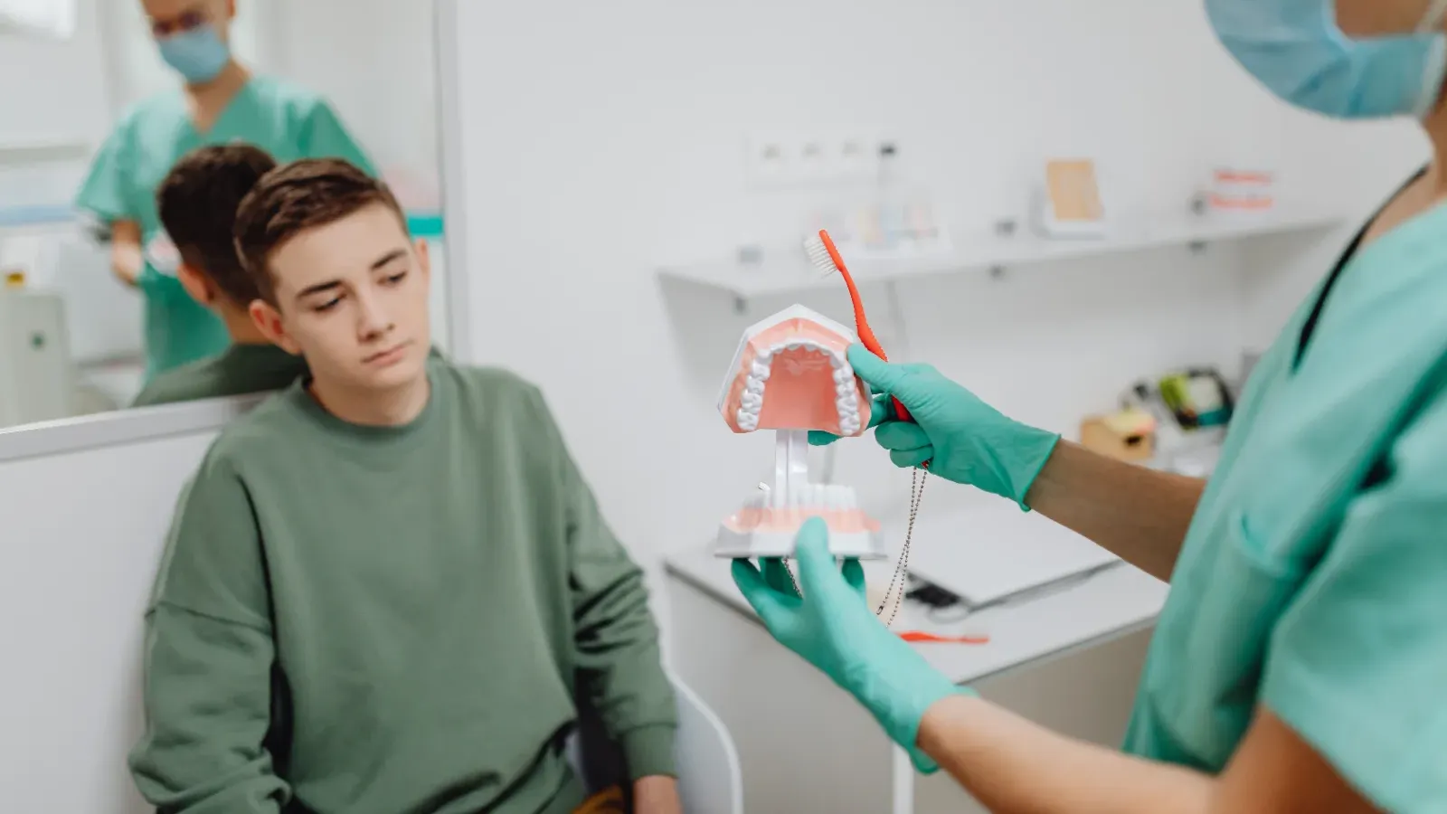 A dental hygienist showing a young patient a model of teeth during a consultation